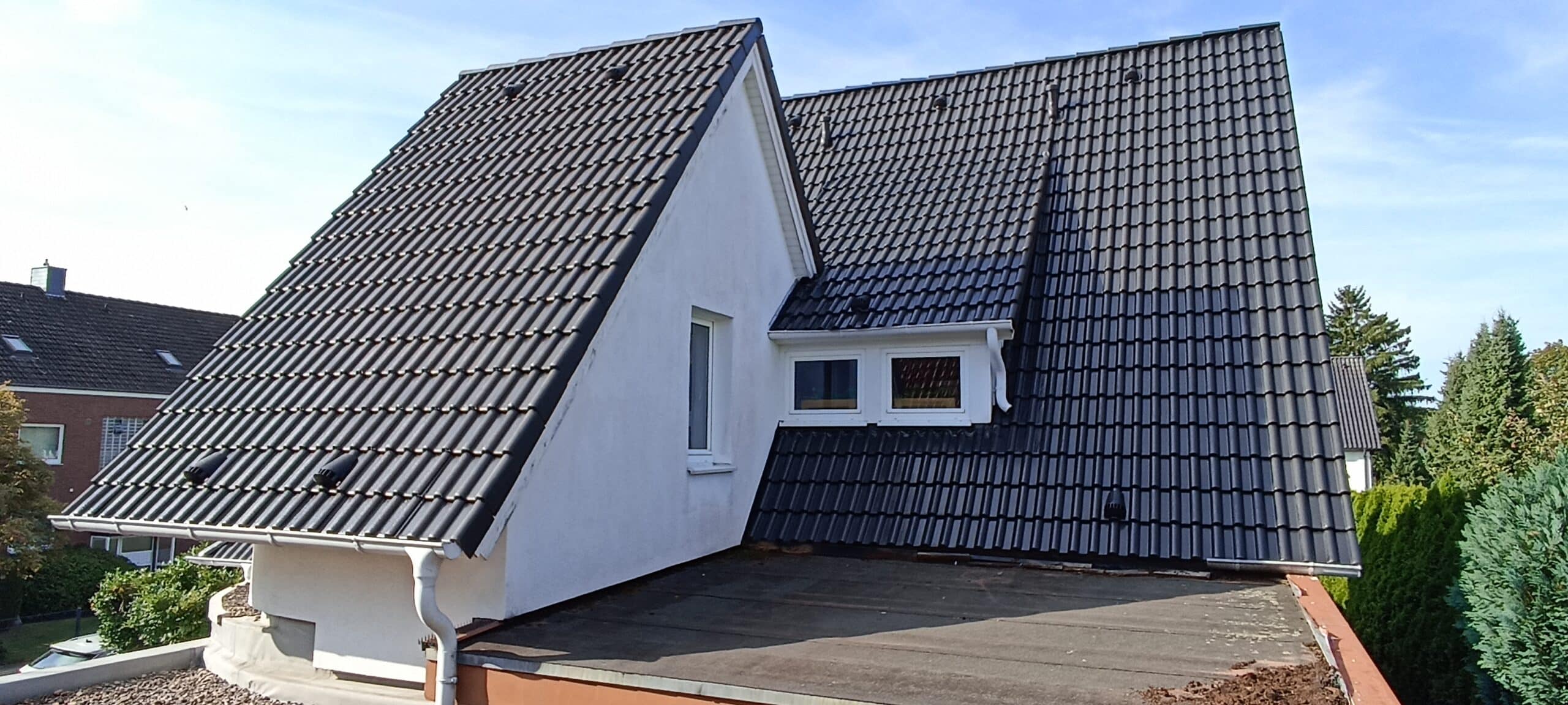 Ein weißes Haus mit einem großen, schrägen Dach aus dunklen Ziegeln und einem kleinen Fenster in einem hellen Garten.