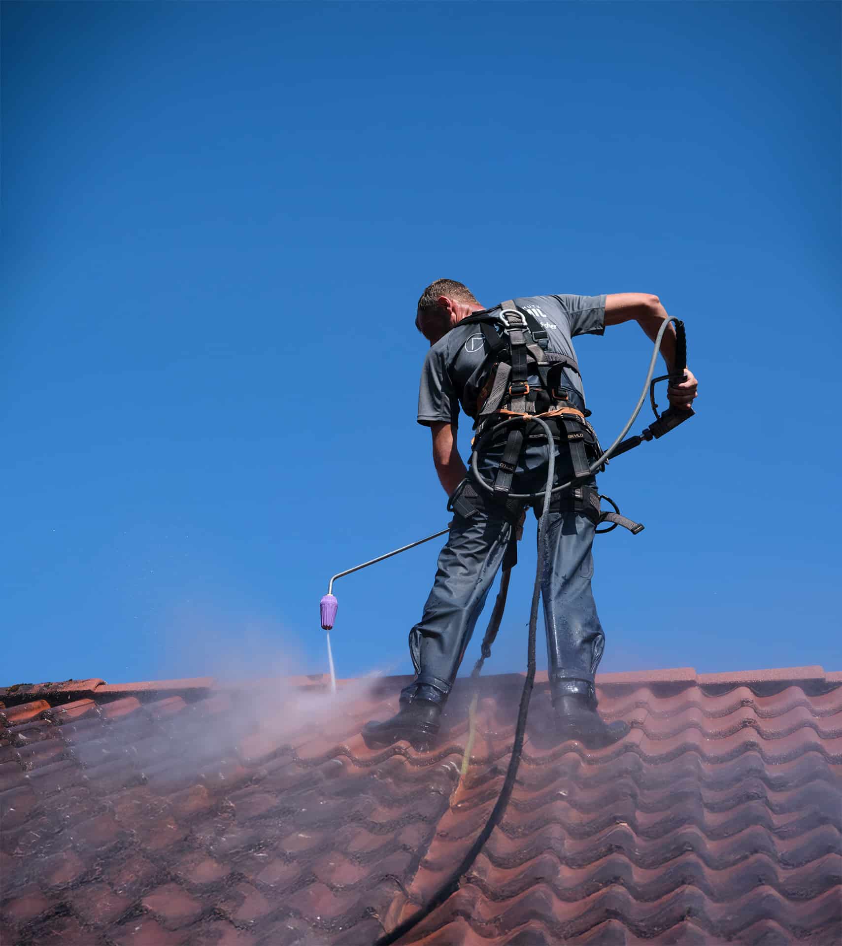 Ein Arbeiter von Bautenschutz Bogumil GmbH reinigt mit Hochdruckreiniger Ziegel auf einem Dach.