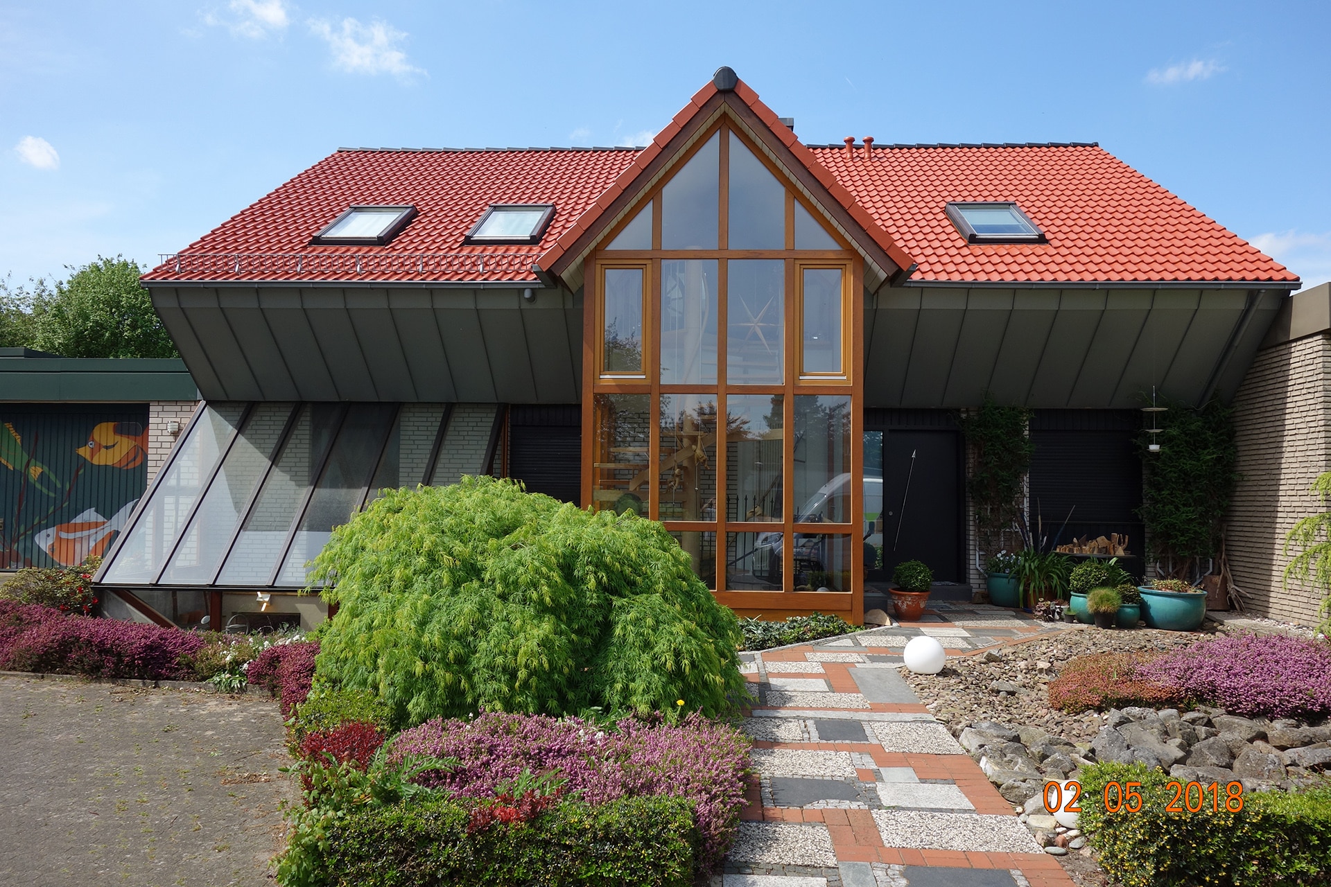 Modernes Gebäude mit rotem Ziegeldach und großem Glasbereich, umgeben von gepflegten Sträuchern, bei Bautenschutz Bogumil GmbH.