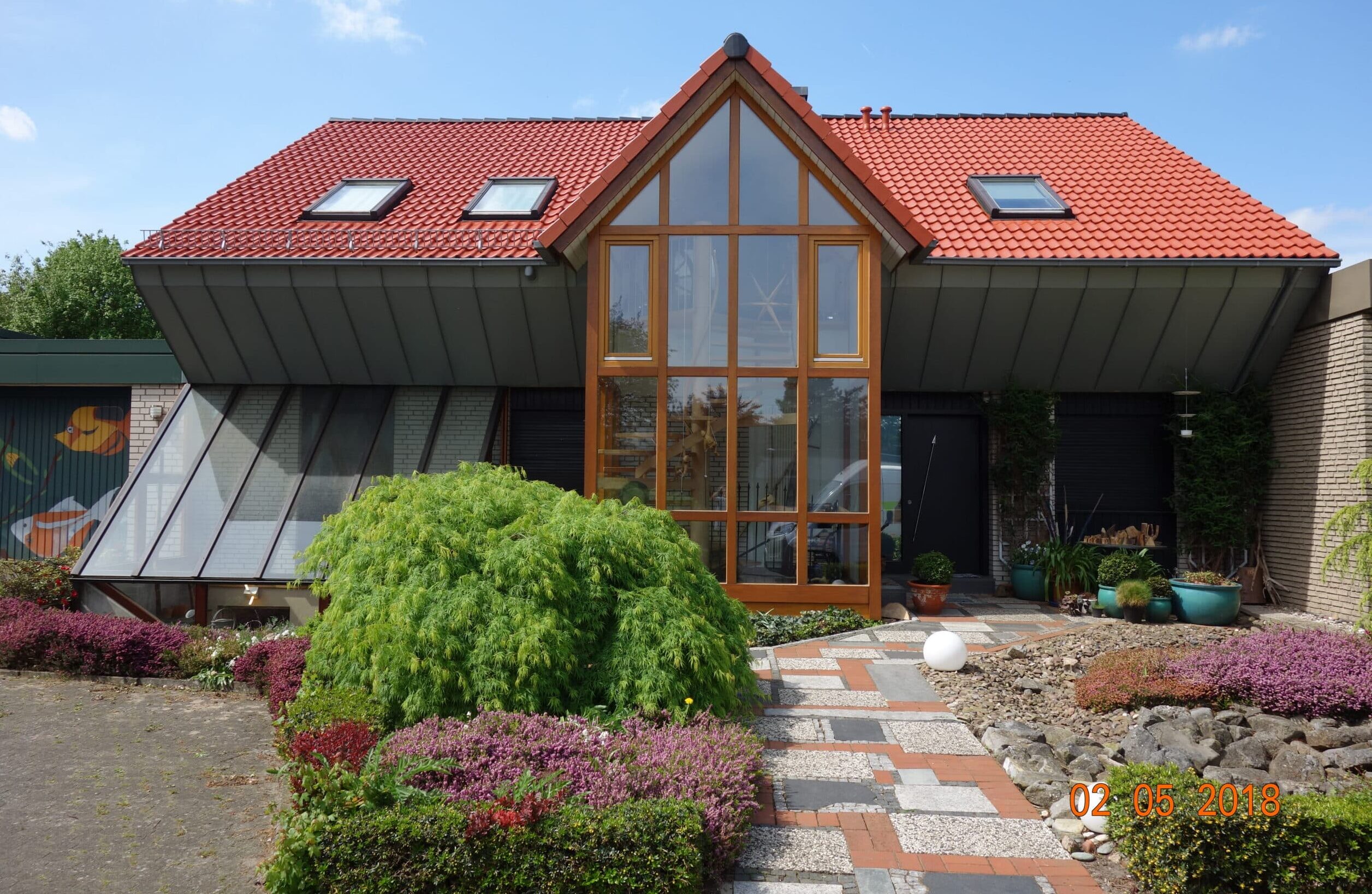 Modernes Gebäude mit rotem Dach und Glasfassade, umgeben von gepflegten Gärten bei Bautenschutz Bogumil GmbH.