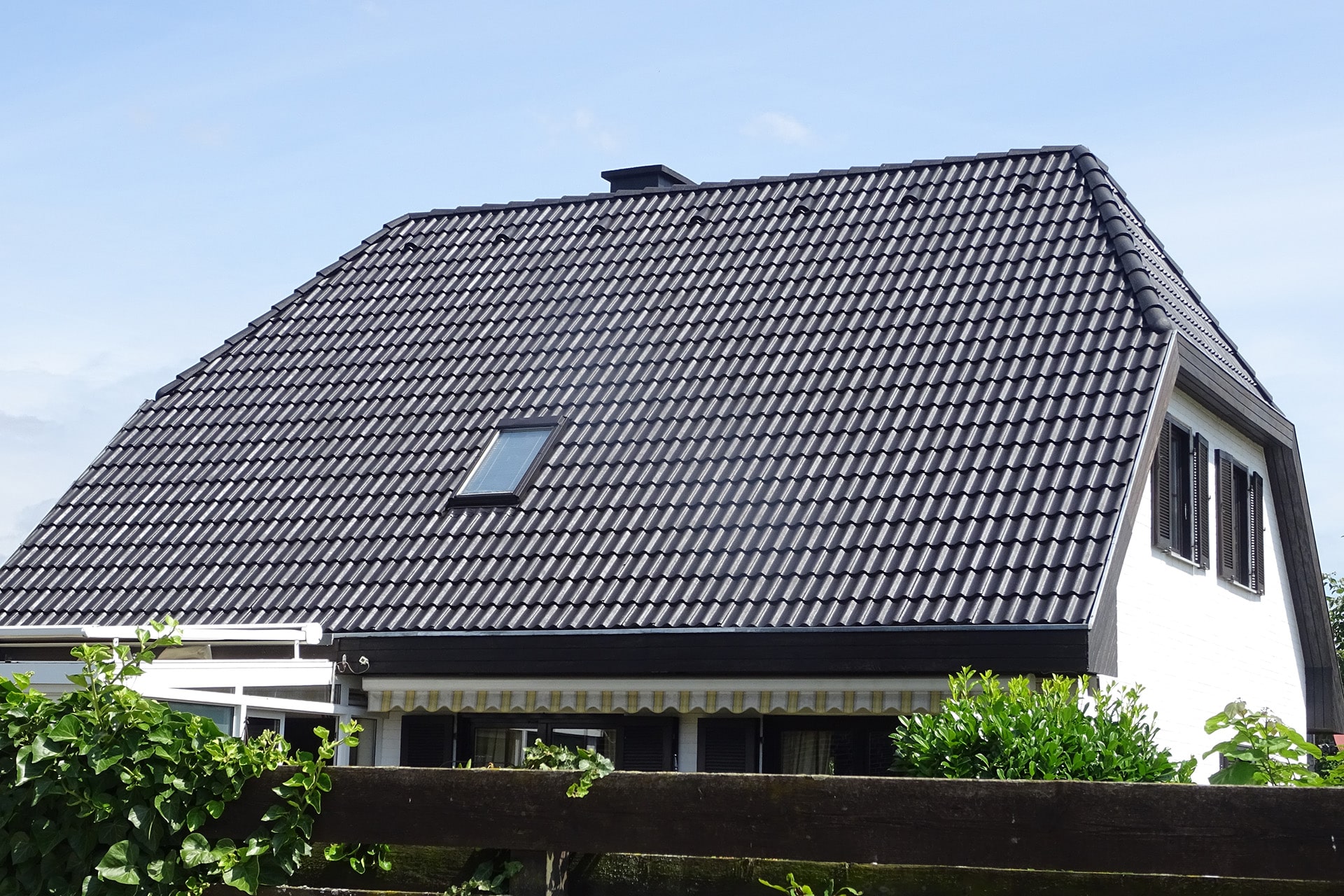 Schwarz gefliestes Dach eines Hauses, behandelt von Bautenschutz Bogumil GmbH, mit Dachfenster unter blauem Himmel.