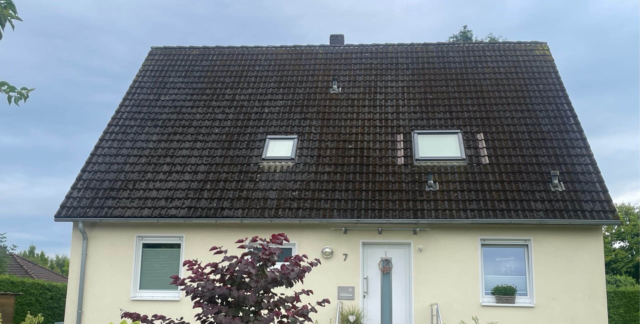 Ein Einfamilienhaus mit einem großen, dunklen Schrägdach, zwei Dachfenstern und einem dekorierten Eingang, umgeben von einem Garten.