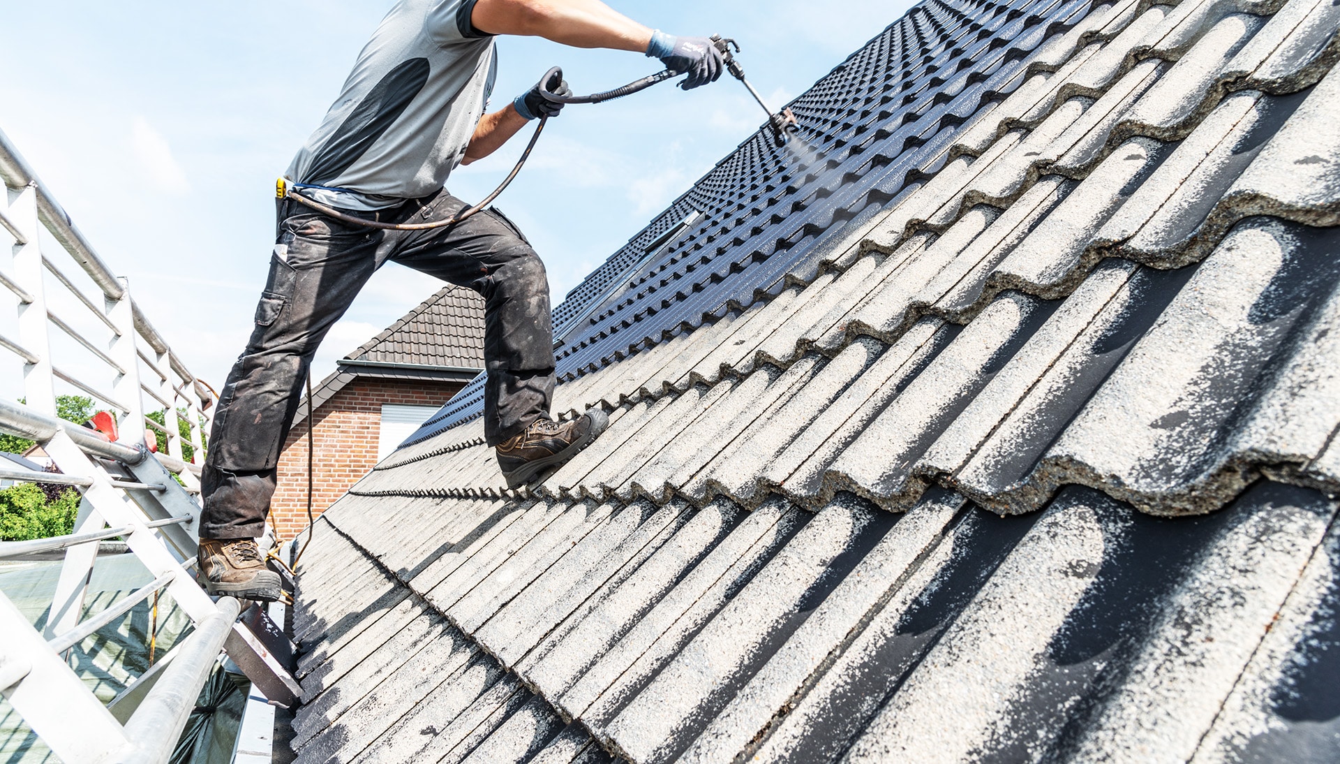 Ein Handwerker reinigt ein Schrägdach mit einem Hochdruckreiniger, im Auftrag von Bautenschutz Bogumil GmbH.