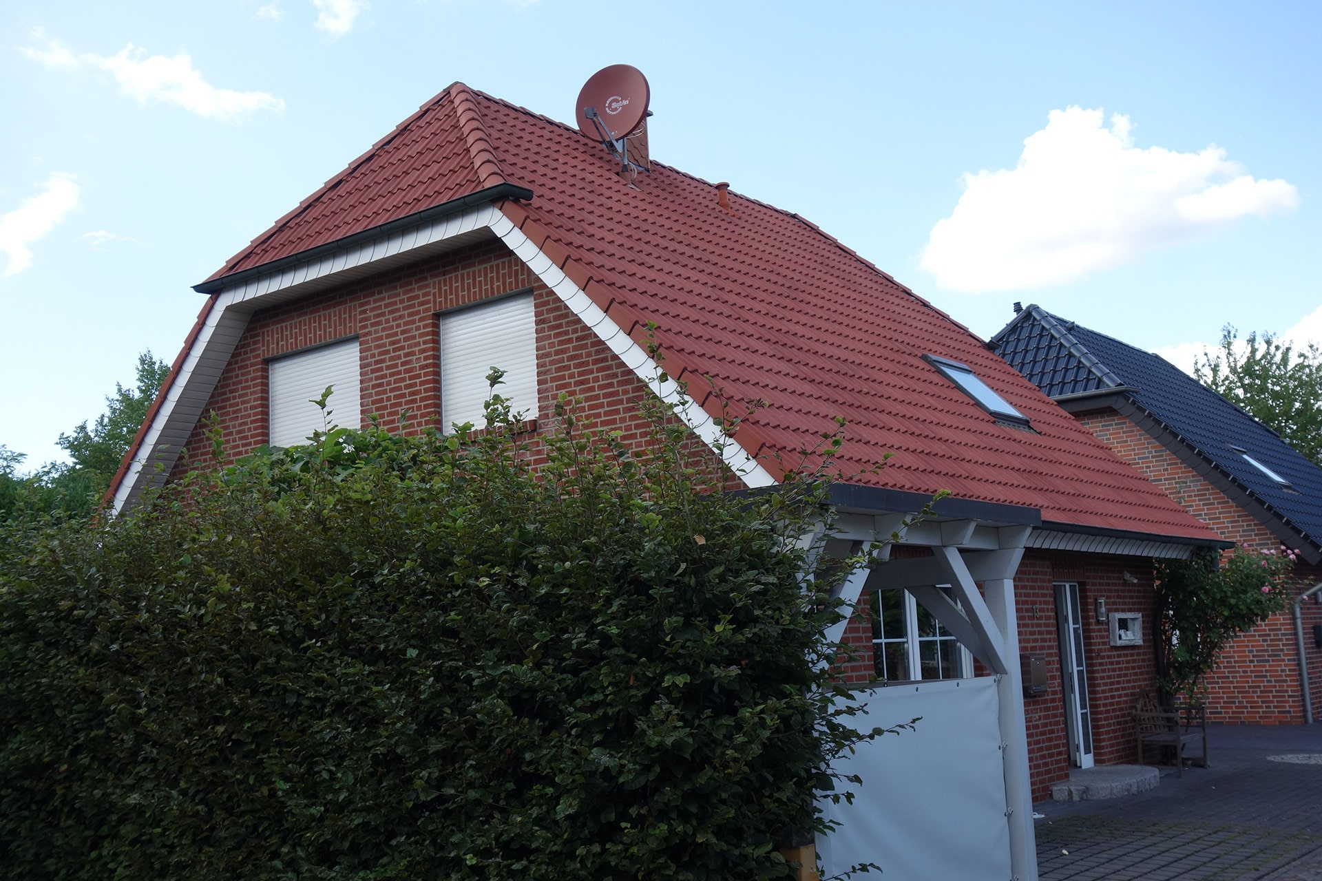 Rotes Ziegeldach eines Backsteinhauses mit Satellitenschüssel, Firma Bautenschutz Bogumil GmbH.